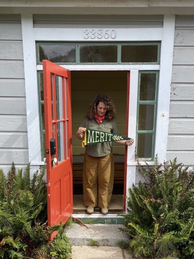 Whitney at the red club door, holding a MERIT pennant